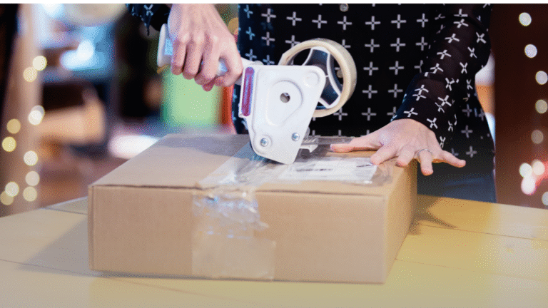 Person using a tape dispenser to seal a cardboard box, illustrating packaging process related to RFID solutions in retail inventory management.