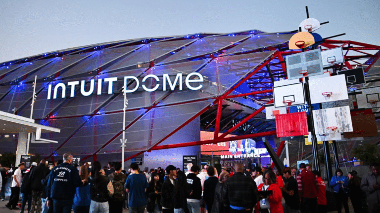 Intuit Dome exterior with illuminated signage, featuring a crowd gathered at the entrance, showcasing the venue's connection to sports and entertainment, relevant to RFID solutions in the sports merchandise retail sector.